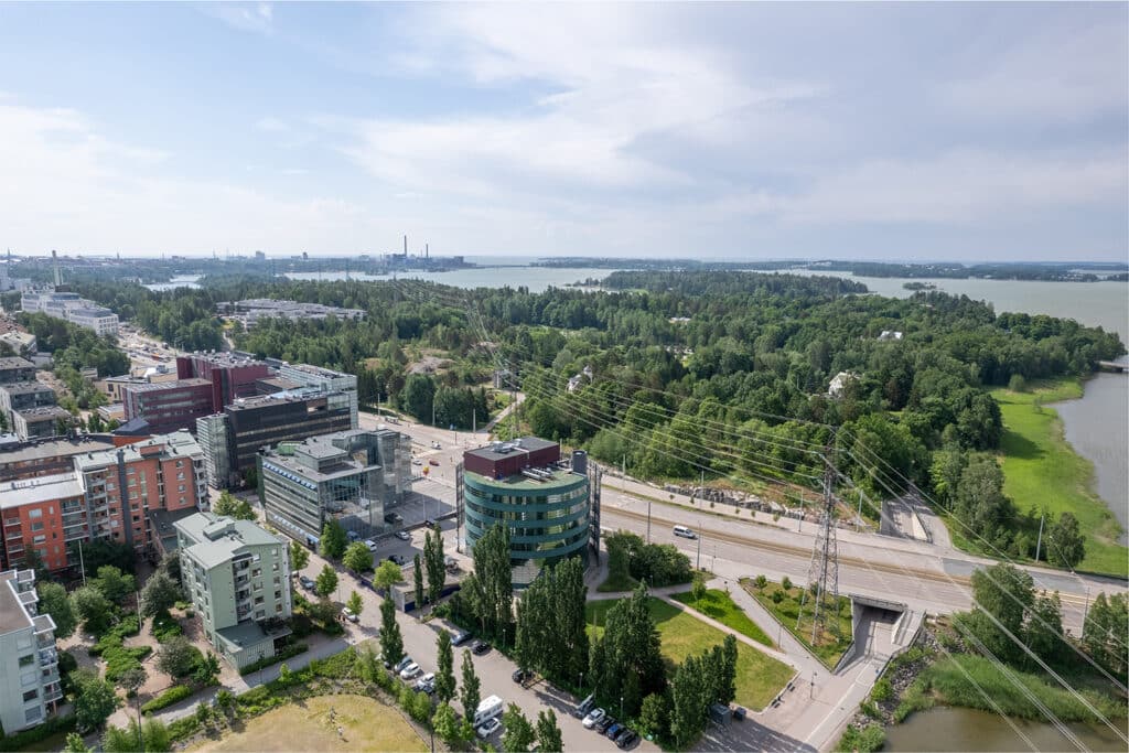 Helsingin Meilahden aluetta ilmasta kuvattuna. Taustalla merta ja Meilahden vehreä arboretum. Etualalla vilkas Paciuksenkatu ja rakennuksia.