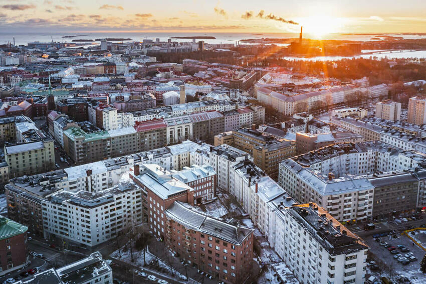 Helsingin keskusta ilmasta kuvattuna, taustalla näkyy meri ja auringonlasku.